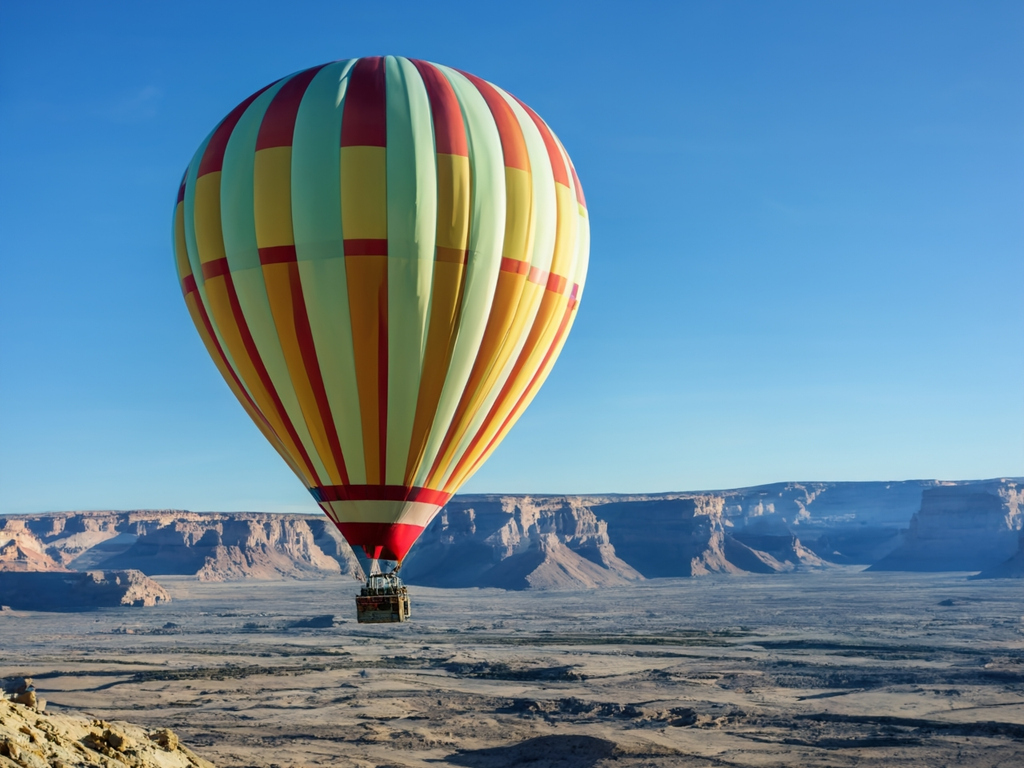 A colourful hot air balloon floats above a rugged desert landscape under a clear blue sky.