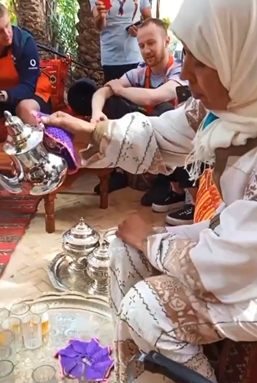 A woman pours tea while others sit nearby, enjoying a traditional gathering.