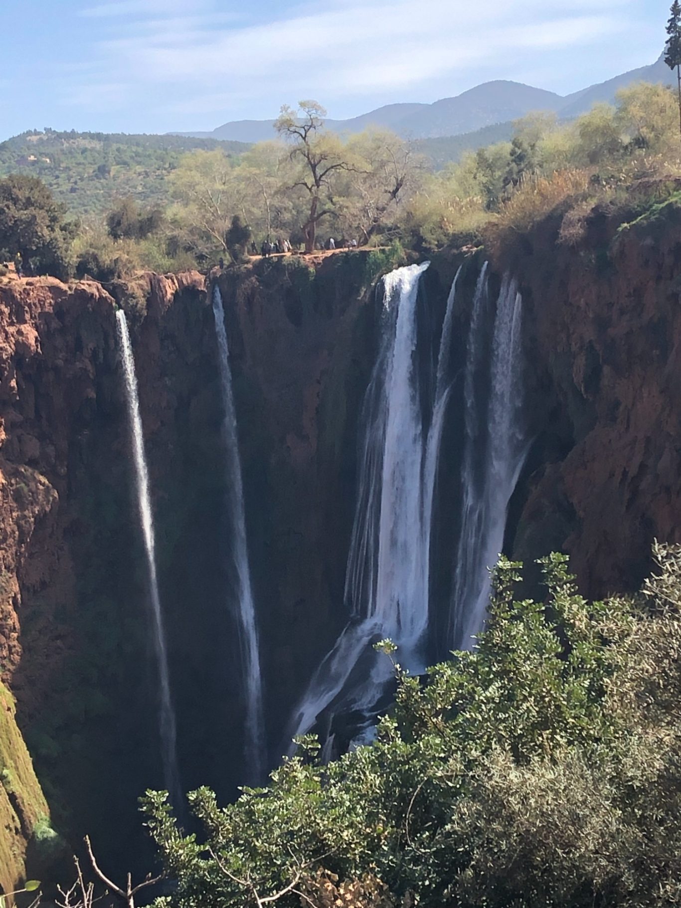 Cascade D'Ouzoud Waterfall A scenic waterfall cascading down rocky cliffs, surrounded by greenery and mountains.